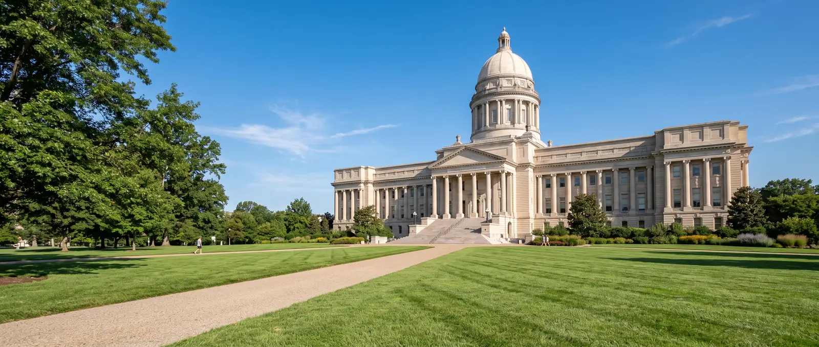 A state capitol under a clear sky, its lawn and path empty in the morning.